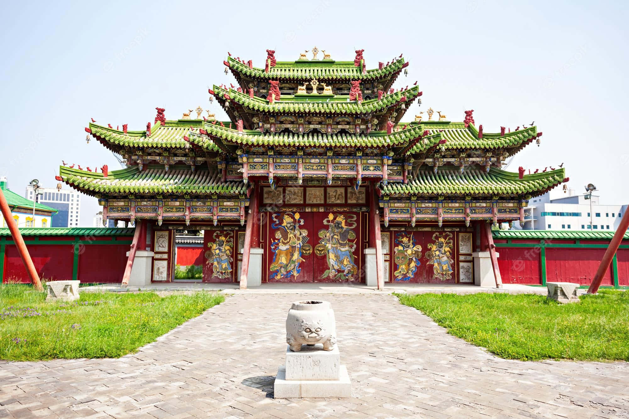 Mongolia 桌布 壁紙 — 一座宏偉的傳統中國寺廟，擁有綠色瓦頂和紅色柱子，矗立在晴朗的天空下，兩側是草地和一條鋪砌小徑上的石獅雕像。