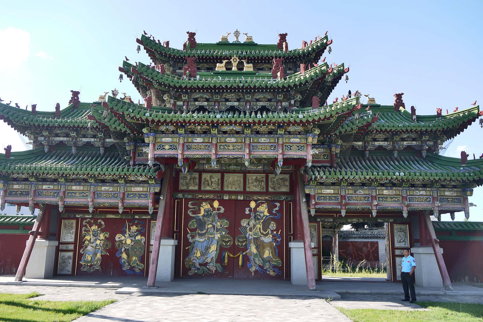 Mongolia 桌布 壁紙 — 一座宏偉的傳統中國寺廟大門，擁有綠色瓦頂和紅色大門，門上飾有守護神壁畫，在清澈的藍天下。