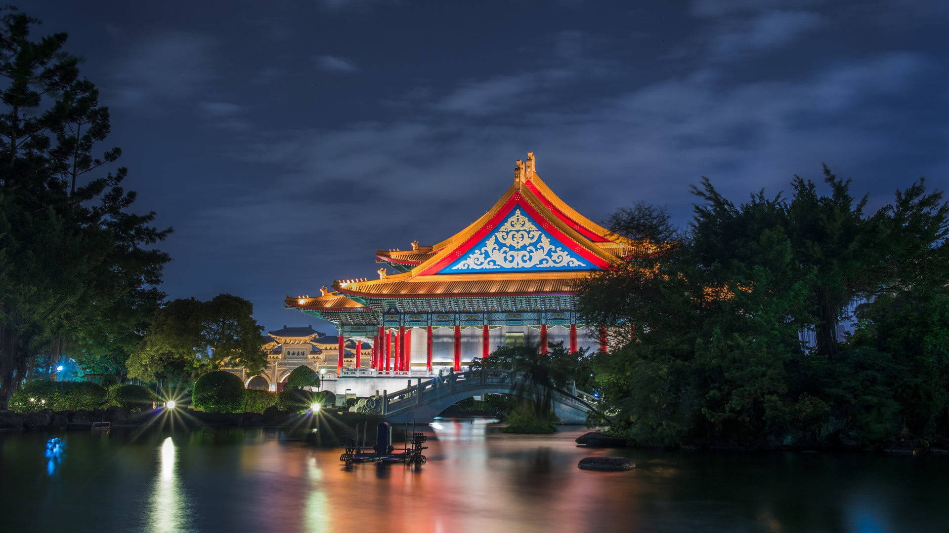 夜間燈火通明的傳統中式亭閣和橋樑倒映在平靜的水面上。