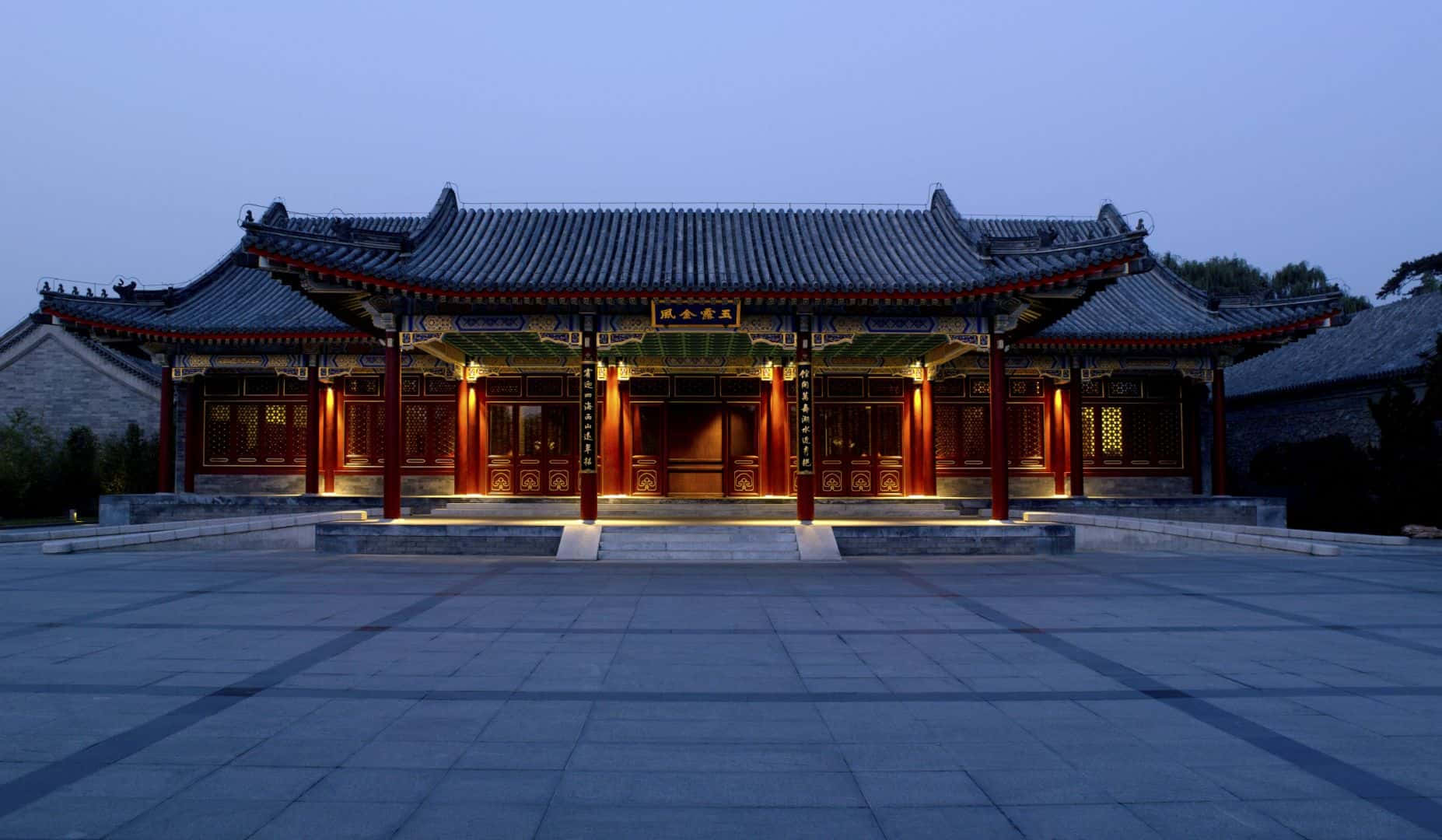 建築 桌布 壁紙 — 一座宏偉的傳統中式亭閣，紅色柱子和瓦片屋頂在暮色天空下溫暖地發光。