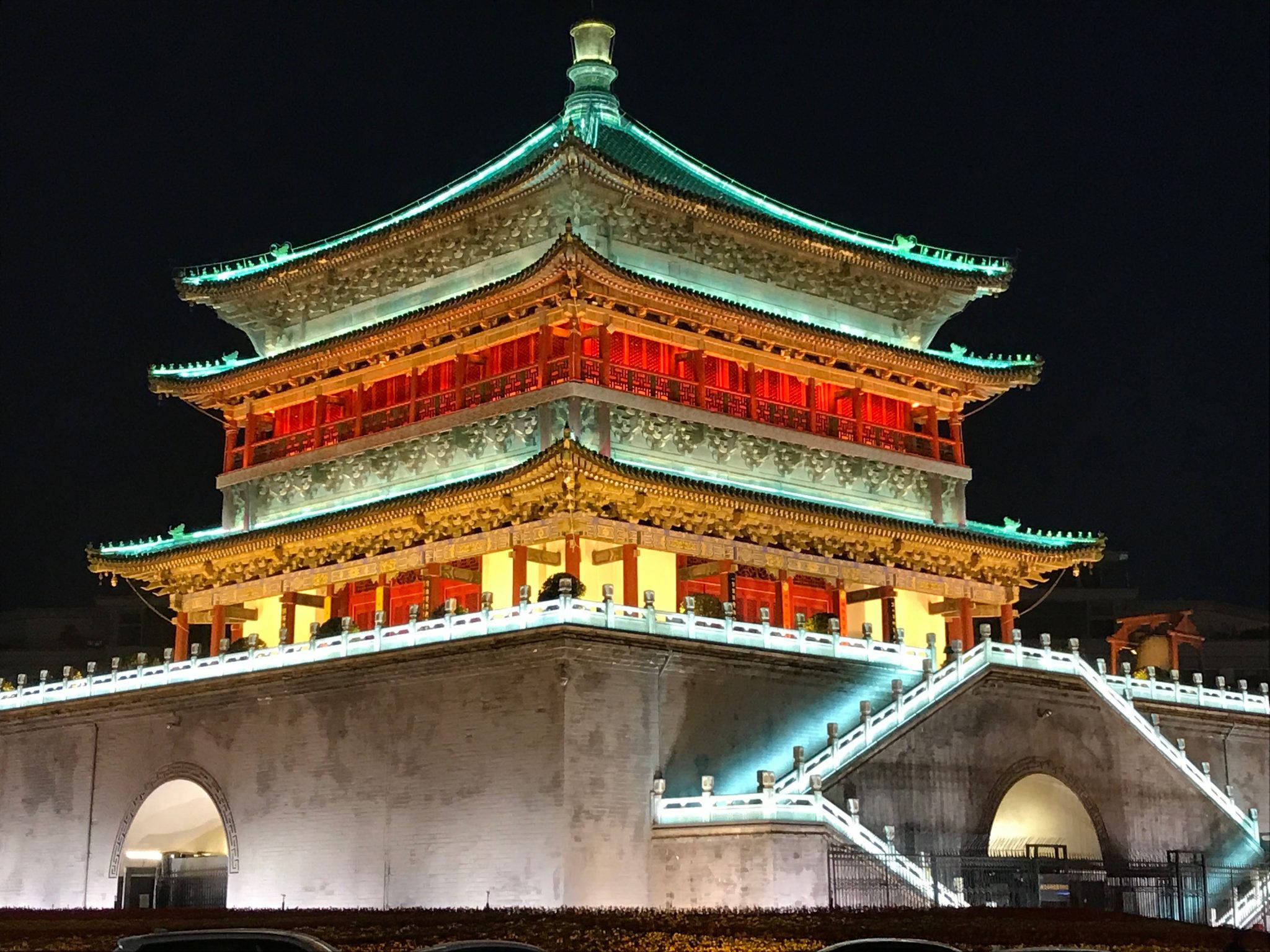 Xian 桌布 壁紙 — 一座宏偉的傳統中式塔樓在夜間被紅色和青綠色的燈光照亮，襯托著黑暗的天空。