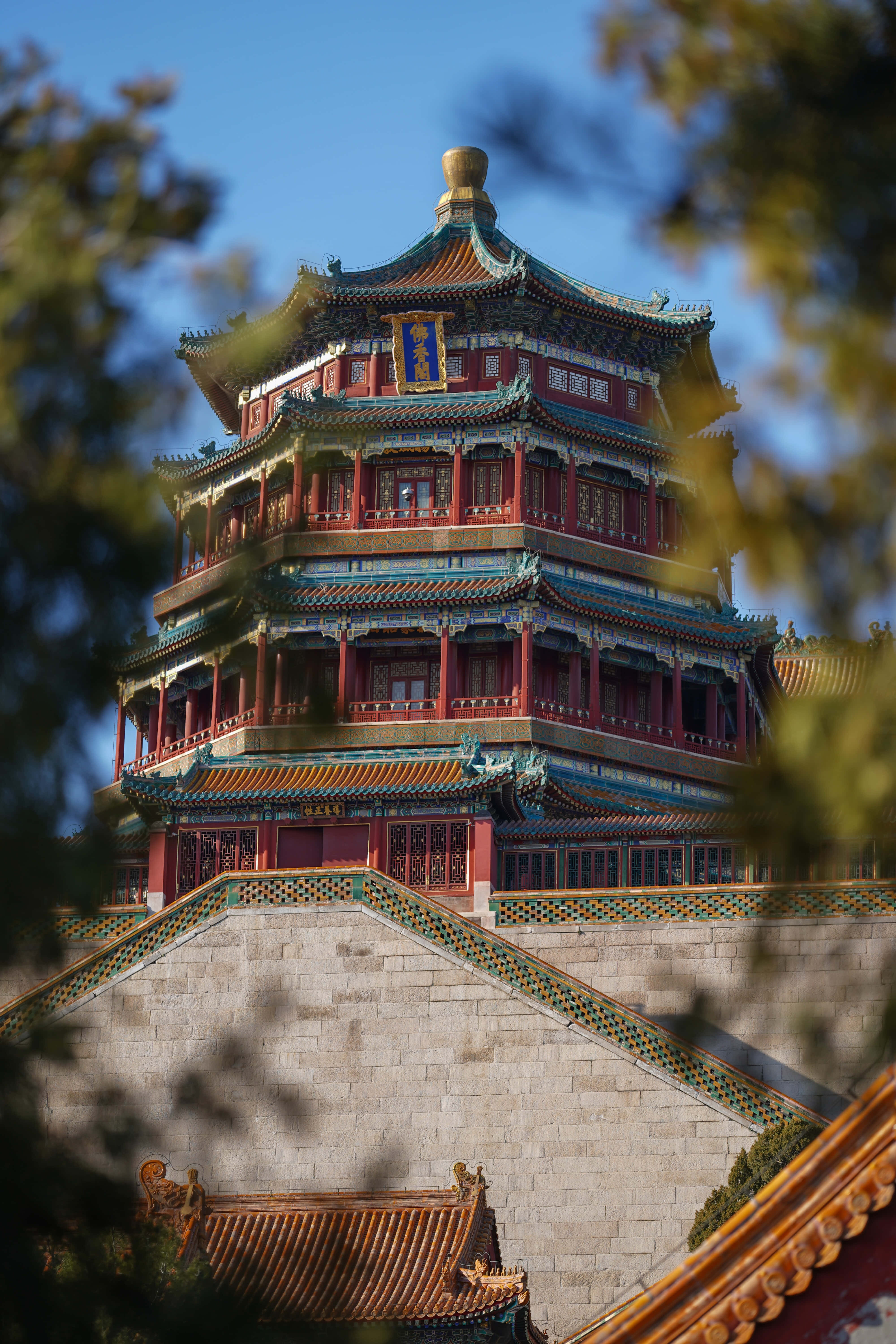 建築 桌布 壁紙 — 一座宏偉的傳統中式寶塔，紅牆金瓦，在晴朗的藍天下被模糊的綠色樹葉襯托著。