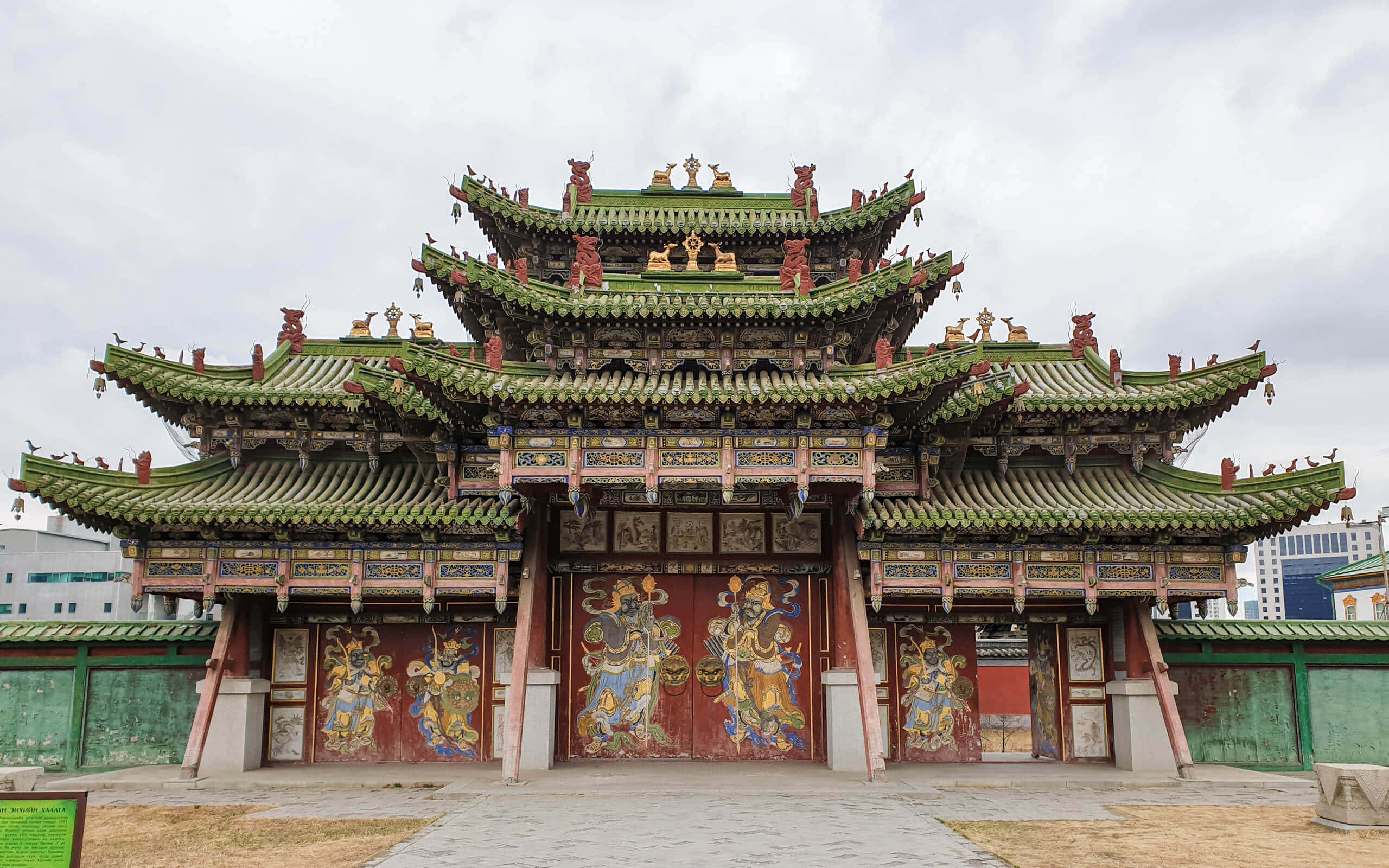 Mongolia 桌布 壁紙 — 一座宏偉的傳統中式寺廟，擁有層層疊疊的綠色屋頂和鮮紅色的門，門上裝飾著色彩繽紛的神明壁畫，天空多雲。