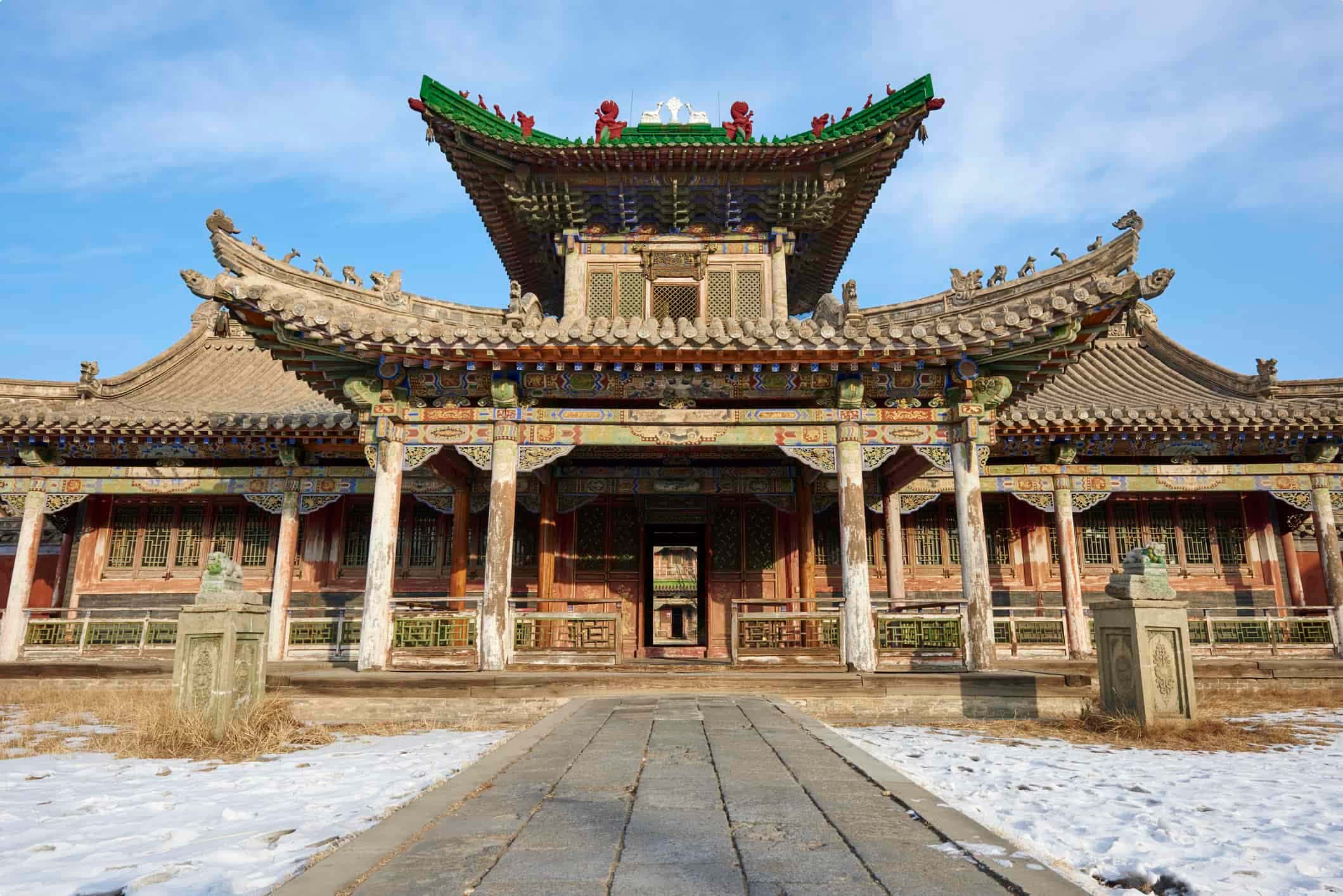 Mongolia 桌布 壁紙 — 一座宏偉的傳統中式寺廟，擁有華麗的綠色屋頂和紅色柱子，矗立在清澈的藍天下，兩側是白雪覆蓋的地面和石獅守護獸。
