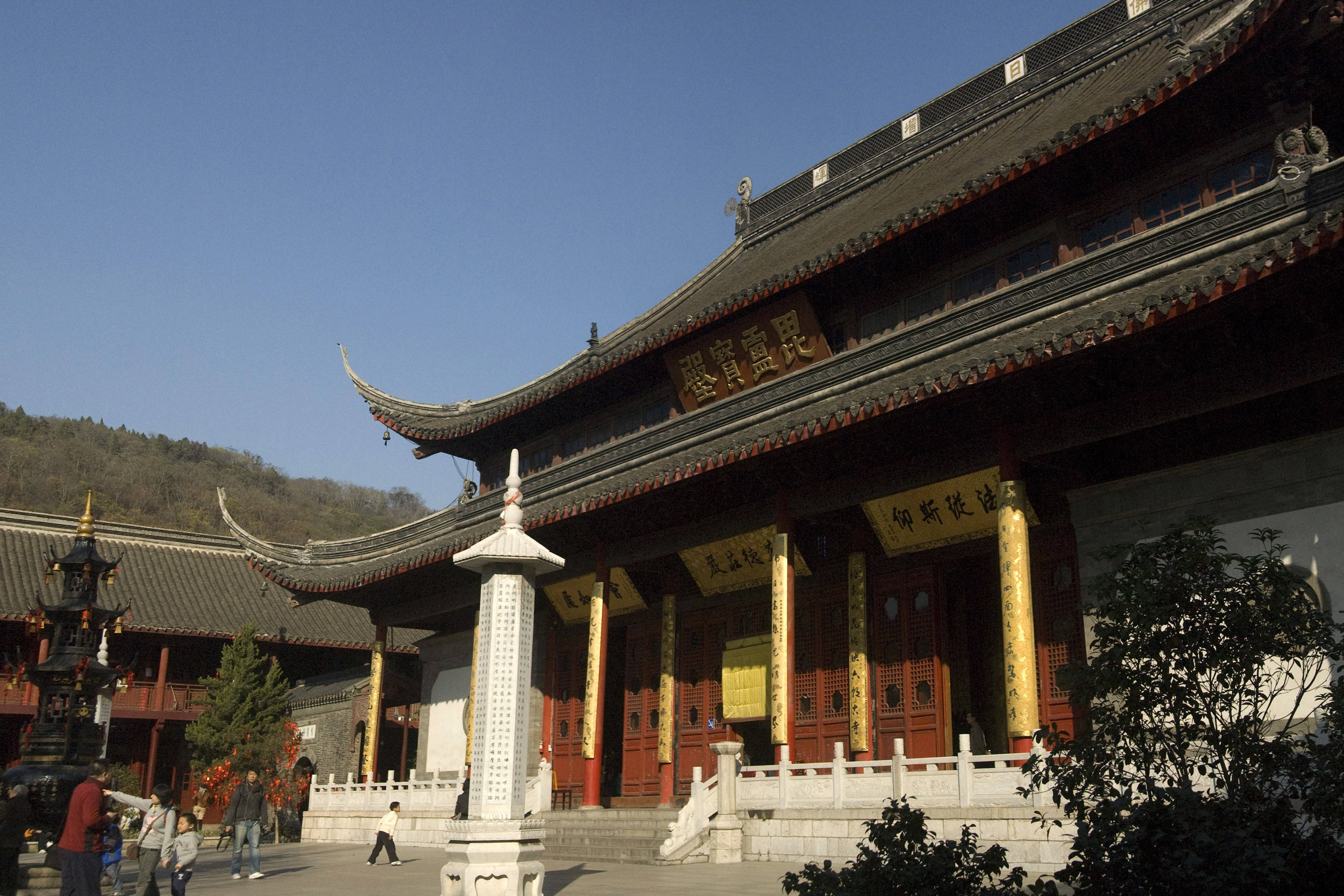 Nanjing 桌布 壁紙 — 一座宏偉的傳統中式寺廟，擁有飛簷翹角的瓦頂和紅色柱子，矗立在晴朗的藍天下，遊客在附近走動。