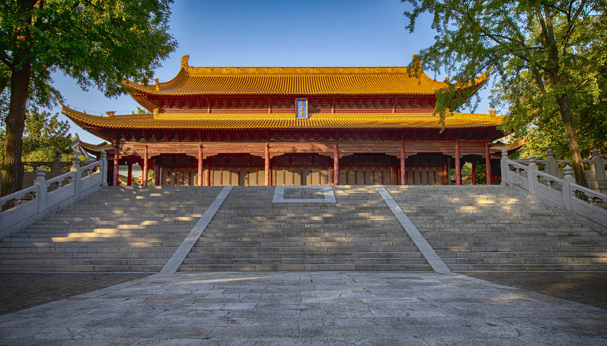 Nanjing 桌布 壁紙 — 一座宏偉的傳統中式寺廟，金色屋頂和紅色柱子矗立在寬闊的石階上，上方是清澈的藍天。