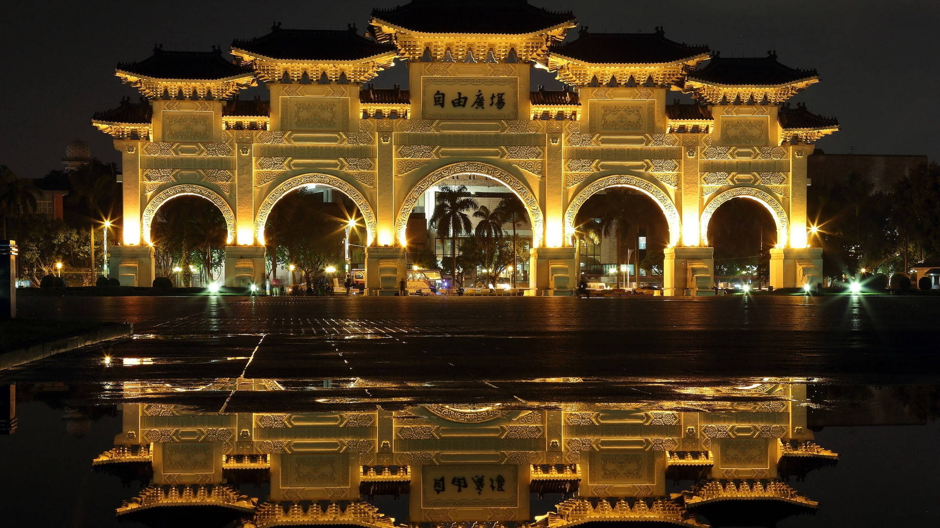 夜晚濕漉漉的路面上倒映著被照亮的傳統中式牌坊。