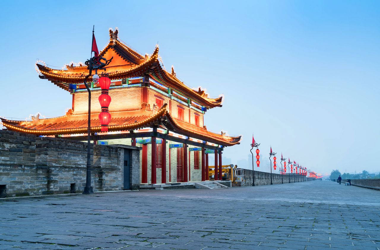 Xian 桌布 壁紙 — 一座宏偉的傳統中式門樓，擁有華麗的瓦頂和紅燈籠，矗立在石牆上，背景是清澈的藍天。
