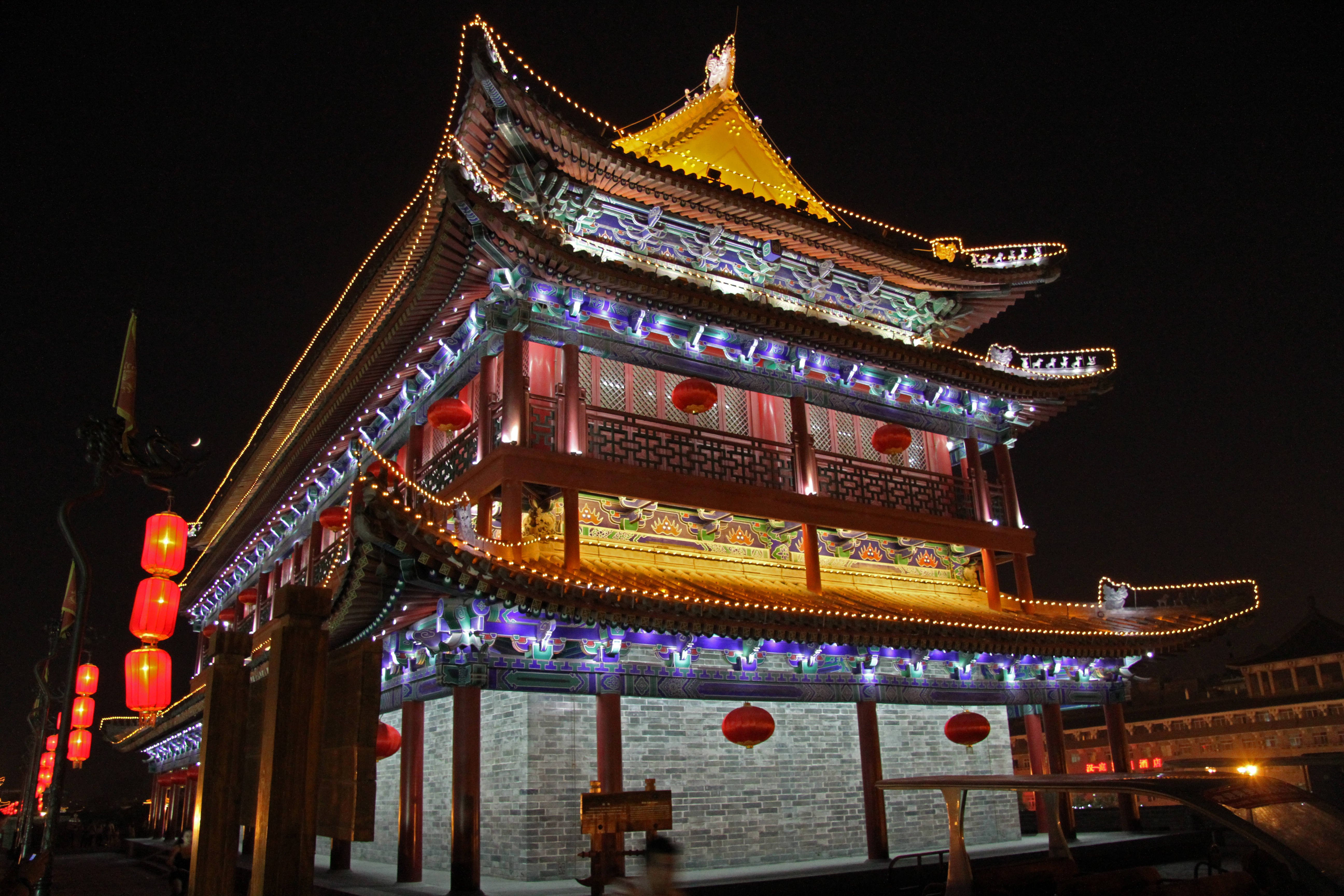 Xian 桌布 壁紙 — 一座宏偉的傳統中式門樓在夜晚被金色燈光、紅色燈籠和彩色燈串照亮，映襯著黑暗的天空。