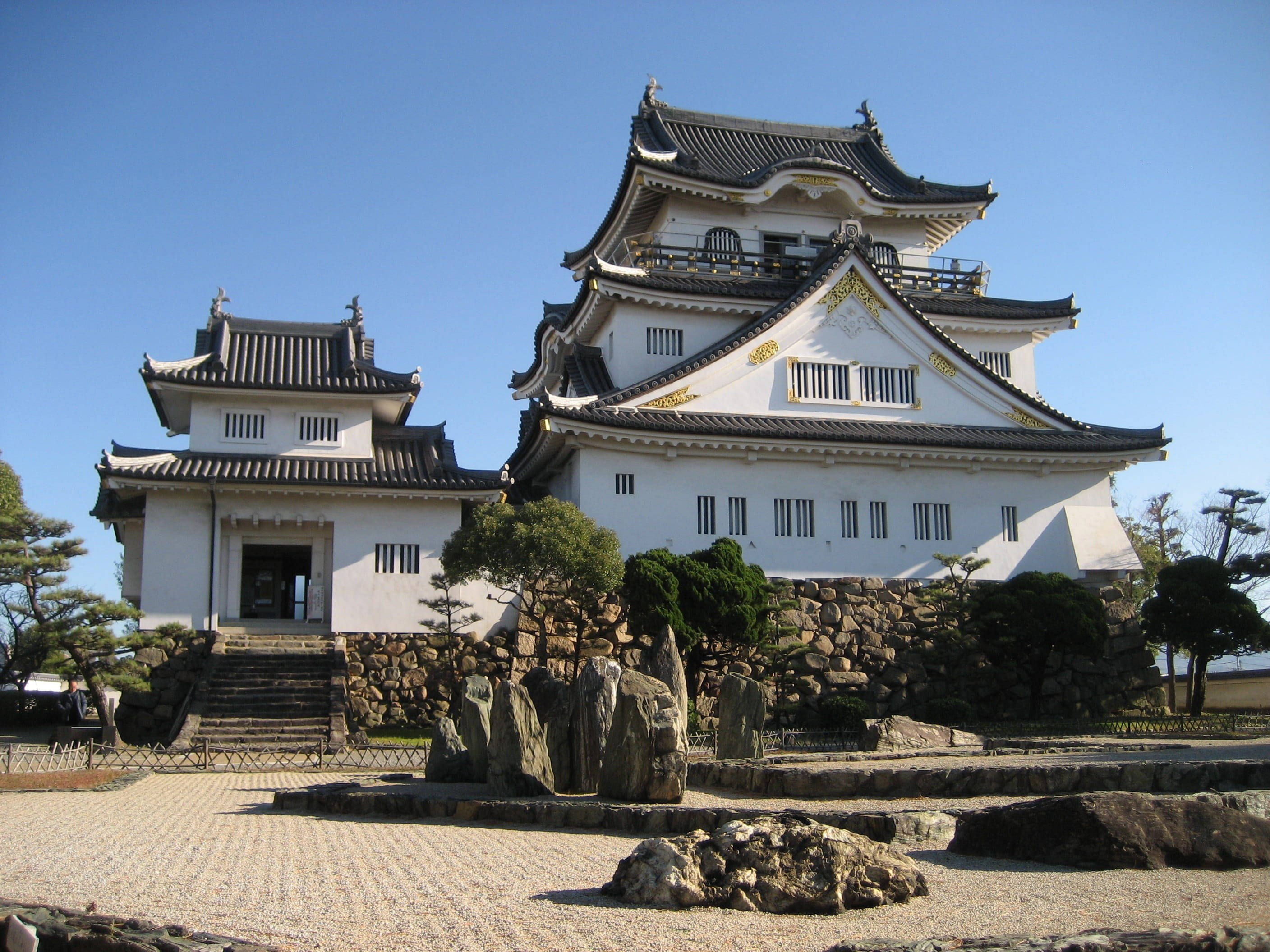 Osaka Castle 桌布 壁紙 — 一座宏偉的傳統日本城堡，白色牆壁和深色瓦片屋頂，在晴朗的藍天下，周圍是修剪整齊的花園和石徑。
