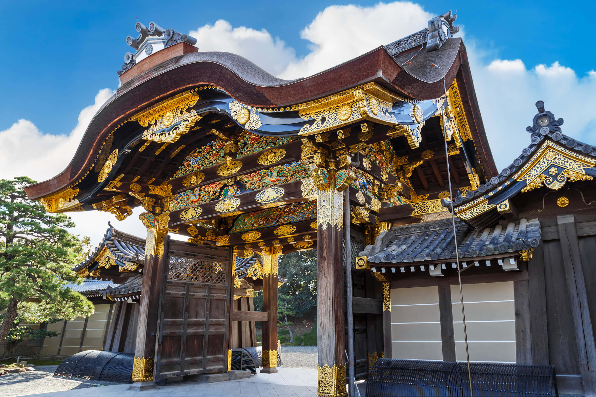 Tokugawa 桌布 壁紙 — 一座宏偉的傳統日本寺廟大門，飾有華麗的金色雕刻和流線型彎曲屋頂，在明亮的藍天下。