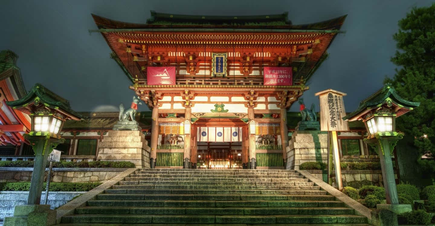 Feudal Japan 桌布 壁紙 — 一座宏偉的傳統日本神社在夜晚被發光的燈籠和通往其華麗木門的石階照亮。