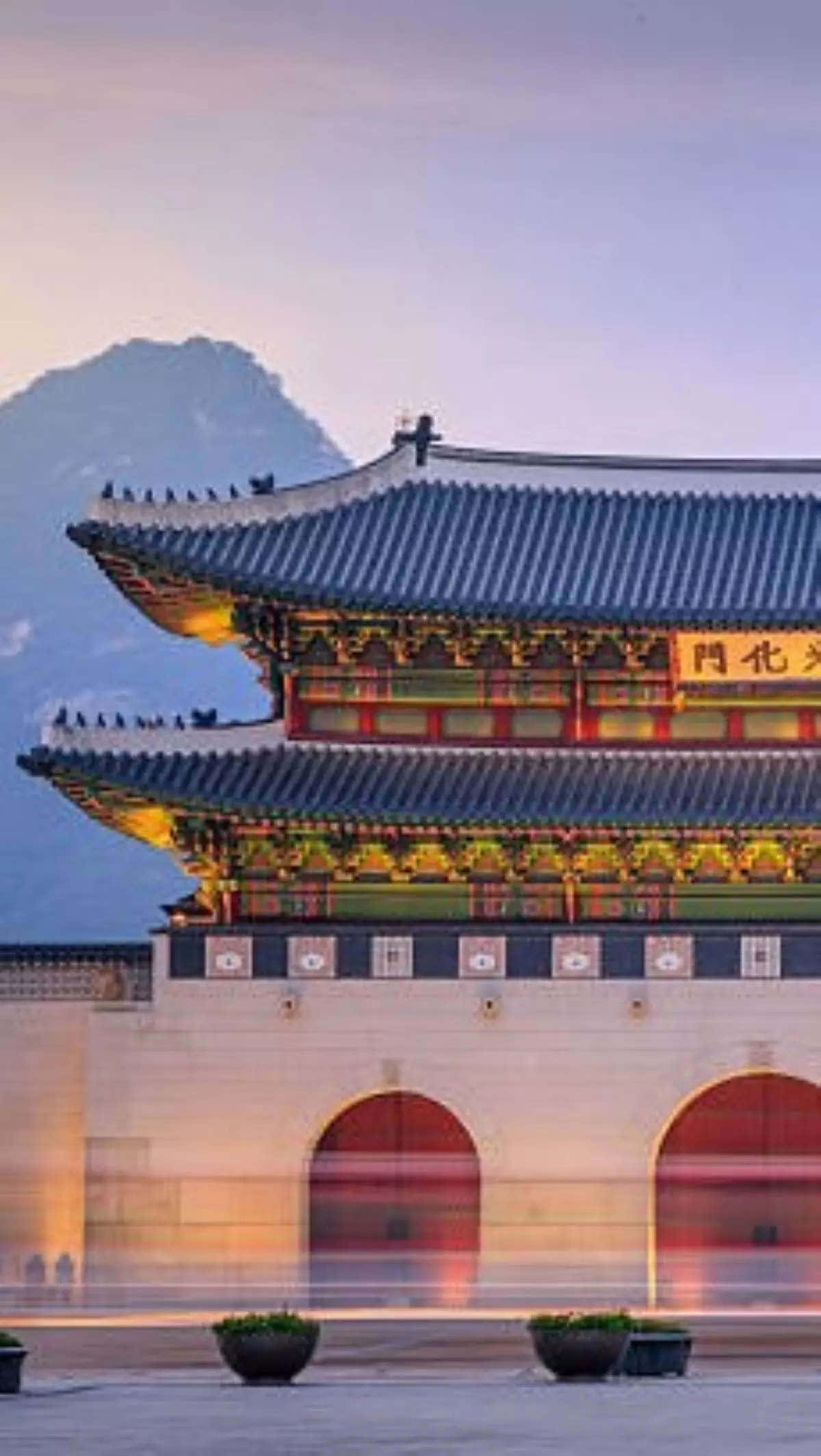 南韓 桌布 壁紙 — 一座宏偉的傳統韓國大門在黃昏時亮起，背景是山脈，下方有模糊的動態。