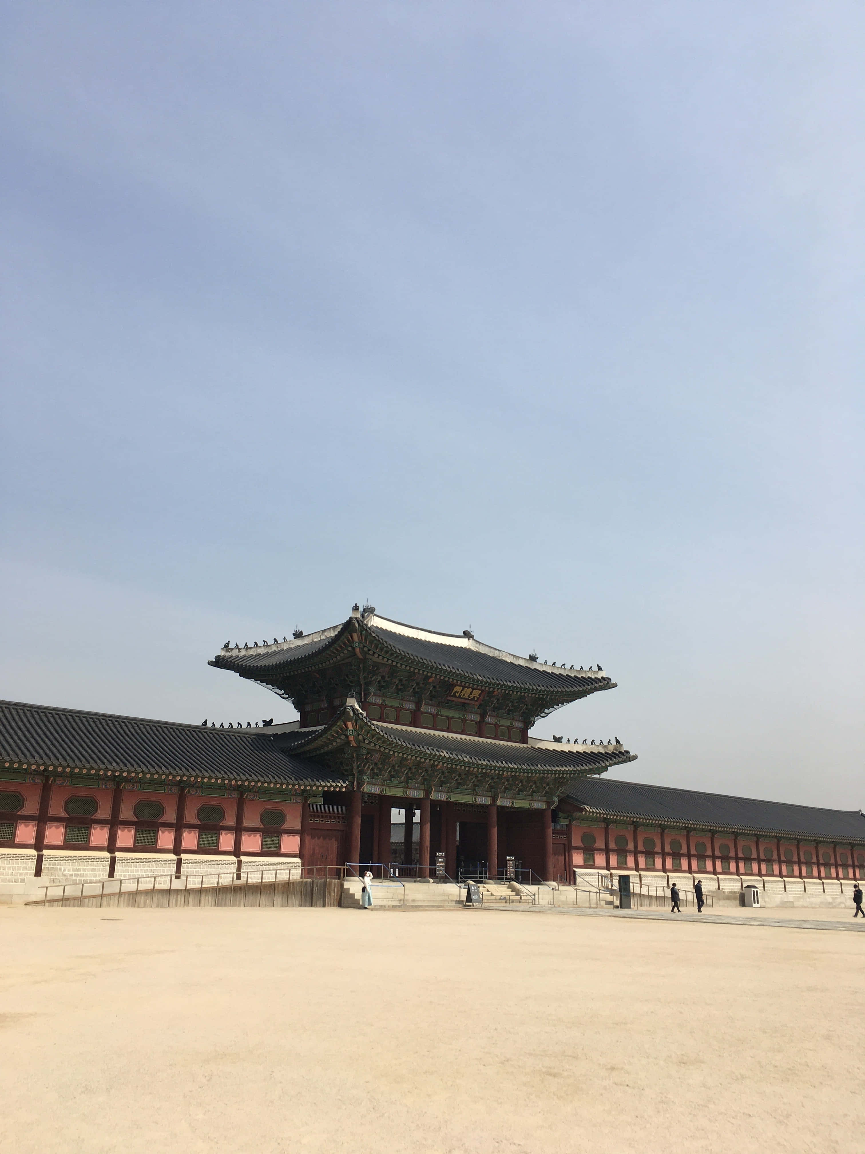 韓國 桌布 壁紙 — 一座宏偉的傳統韓國宮殿，擁有紅牆和彎曲的黑色瓦片屋頂，在晴朗的藍天下。