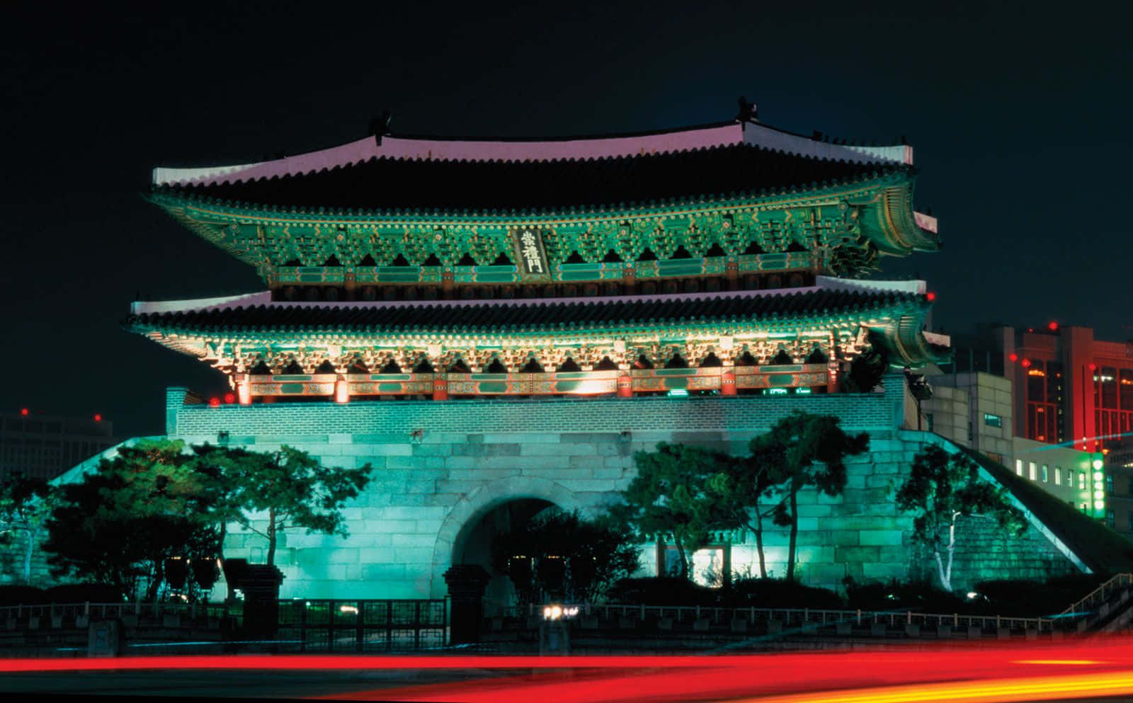 南韓 桌布 壁紙 — 一座宏偉的傳統韓國門樓在夜晚以綠色和紅色燈光照明，下方有汽車燈光形成的條紋。