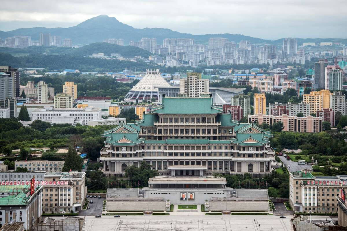 韓國 桌布 壁紙 — 一座宏偉的傳統風格建築，擁有綠色屋頂，在陰天和遠處山巒的襯托下，主導著城市景觀。