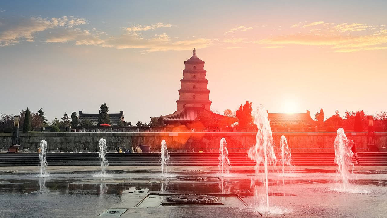 Xian 桌布 壁紙 — 一座宏偉的古塔在溫暖的日落天空下呈現剪影，前景中噴泉噴灑著水花。