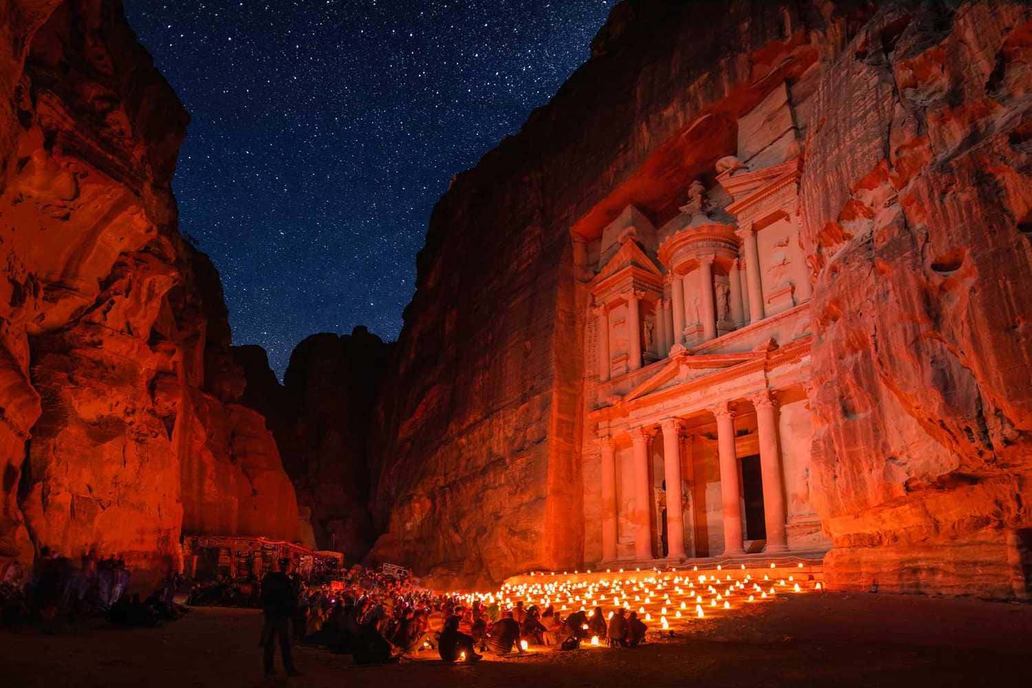 Jordan 桌布 壁紙 — 一座宏偉的古老寺廟雕刻在懸崖上，在星空下溫暖地發光，人群聚集在閃爍的蠟燭周圍。