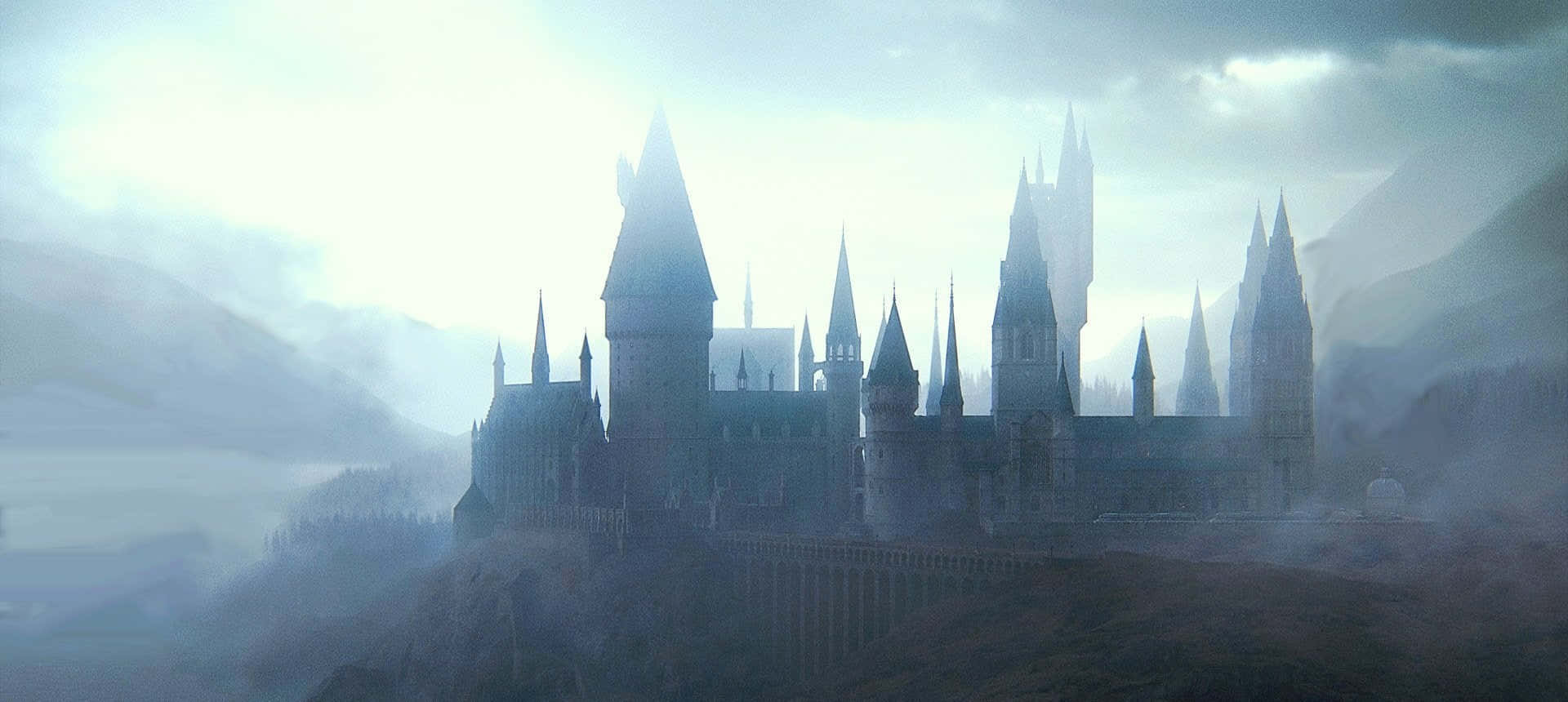 Harry Potter Halloween 桌布 壁紙 — 一座宏偉的哥德式城堡，尖塔從雲霧繚繞的山峰上聳立，天空多雲。