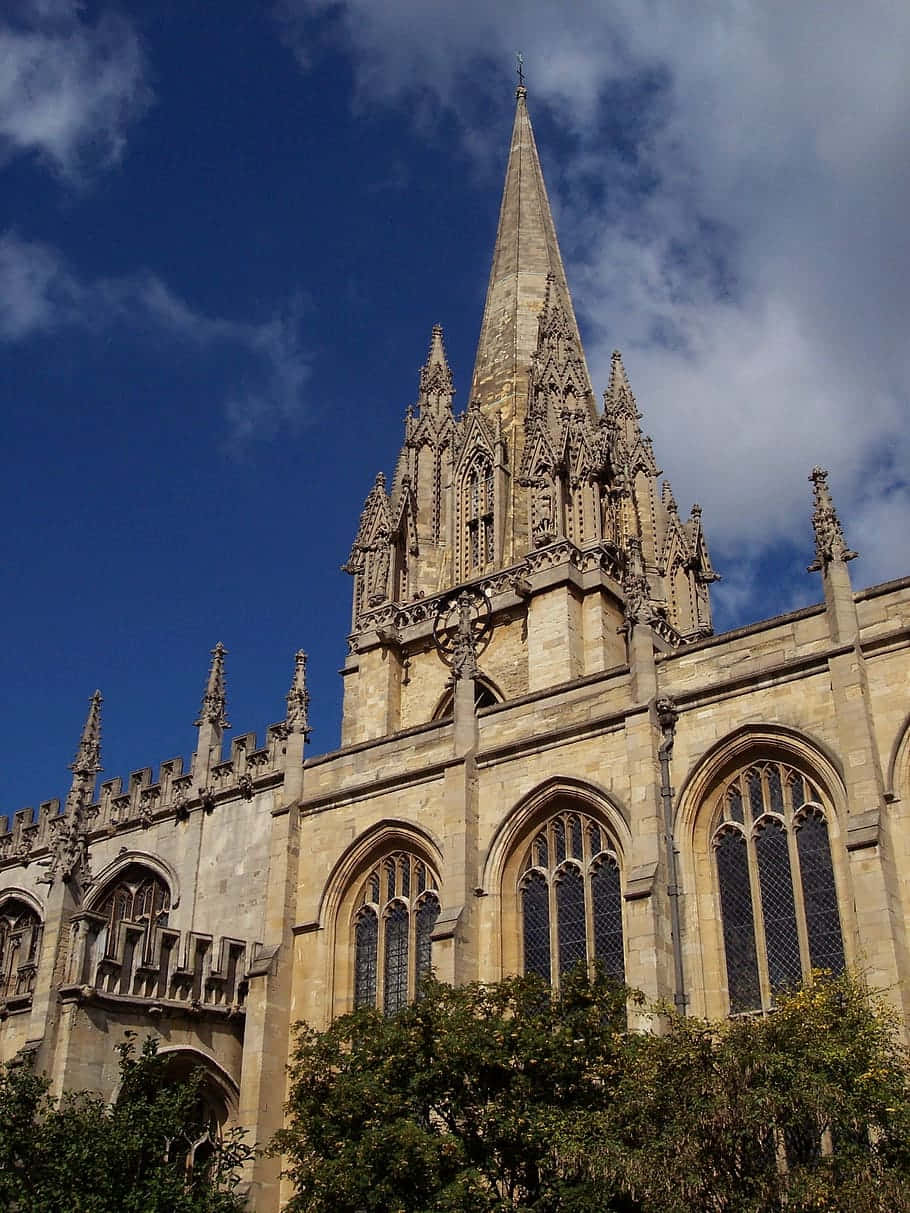 England 桌布 壁紙 — 一座宏偉的哥德式大教堂，擁有高聳的尖塔和精緻的石雕，矗立在蔚藍的天空和散落的雲朵下。