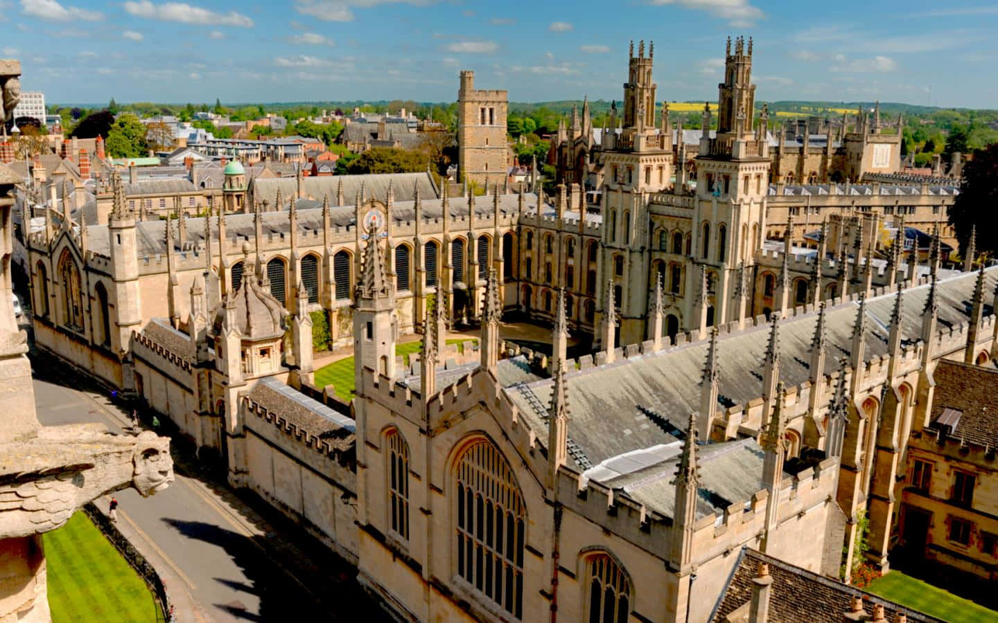England 桌布 壁紙 — 一座宏偉的哥德式大教堂的鳥瞰圖，擁有尖塔和石造建築，在明亮的藍天下有零星雲朵。