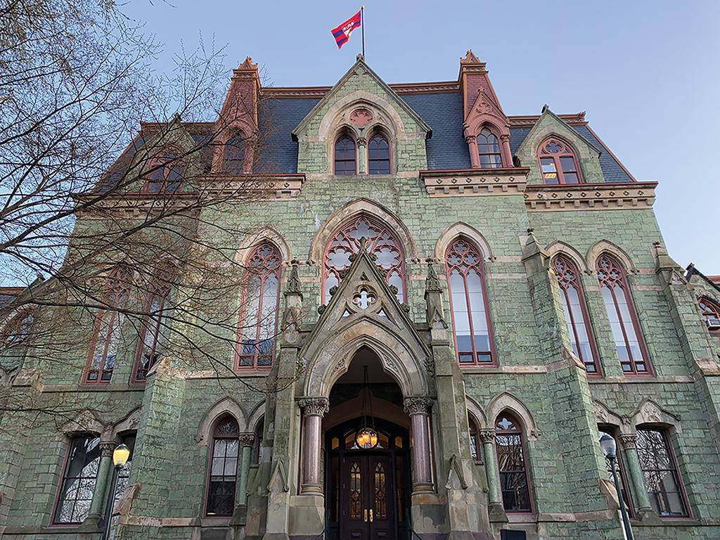 University Of Pennsylvania 桌布 壁紙 — 一座宏偉的哥德復興式石建築，擁有綠色牆壁、紅色飾邊和拱形窗戶，在清澈的藍天下。