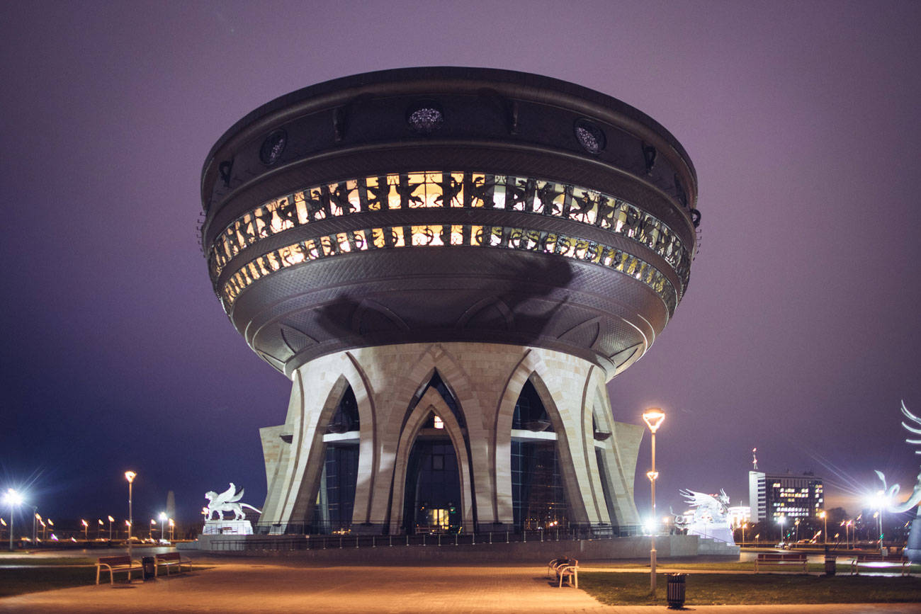 Kazan 桌布 壁紙 — 一座宏偉的圓形建築在夜晚亮起燈光，拱形支撐結構在紫色天空下散發溫暖光芒。