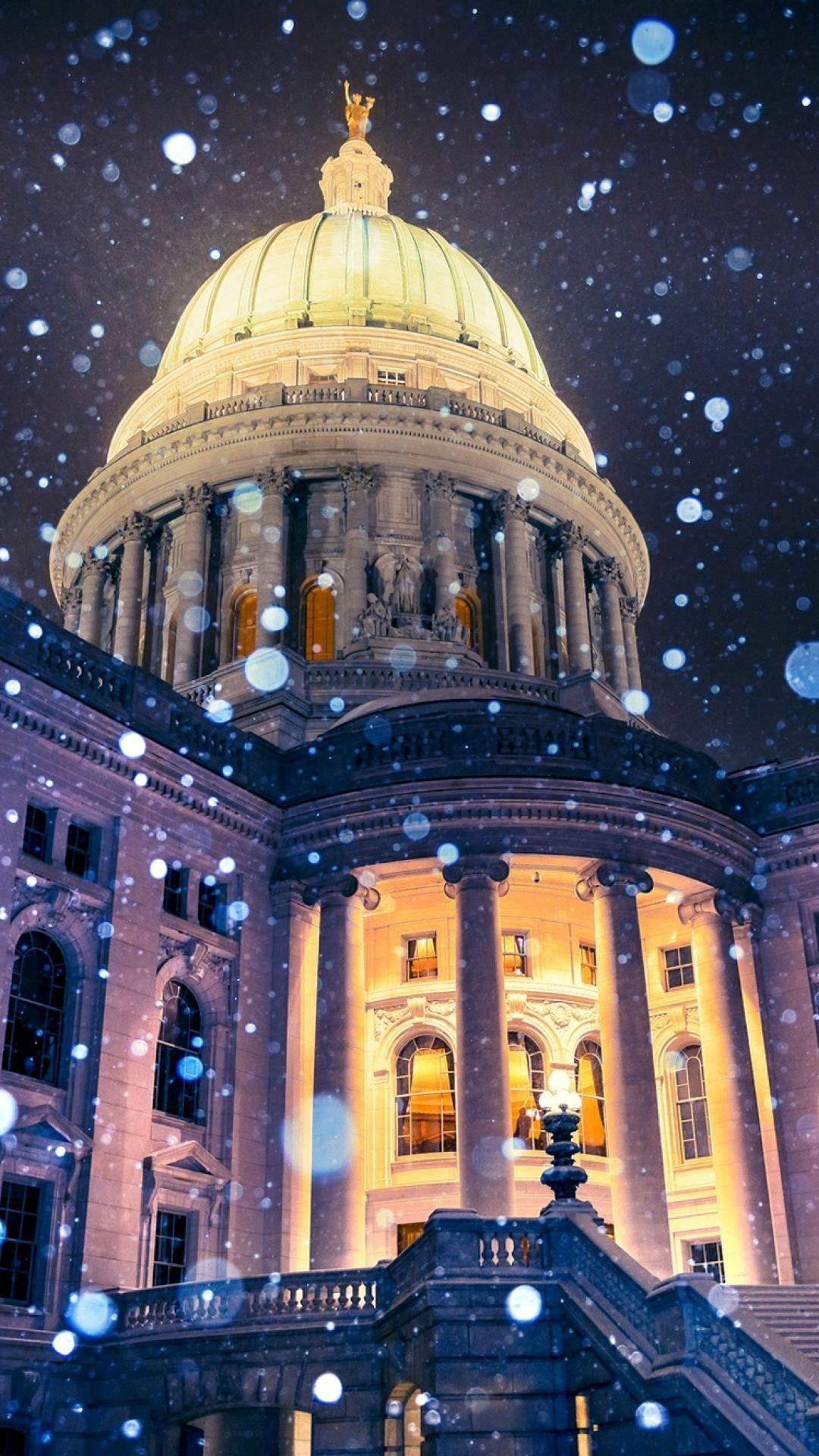 建築 桌布 壁紙 — 一座宏偉的圓頂國會大廈在飄雪的夜空下，伴隨著飄落的雪花和散景燈光，散發出溫暖的光芒。