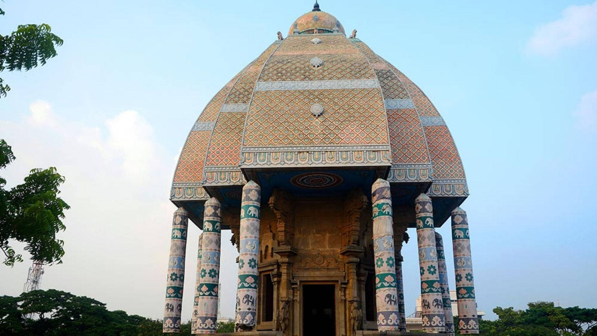 Chennai 桌布 壁紙 — 一座宏偉的圓頂寺廟，帶有複雜的瓷磚圖案和彩繪柱子，在清澈的藍天下高高聳立。