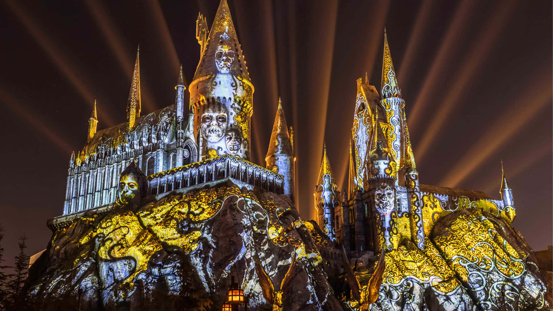 Hogsmeade 桌布 壁紙 — 一座宏偉的城堡，帶有骷髏投影和金色光束，照亮夜空。