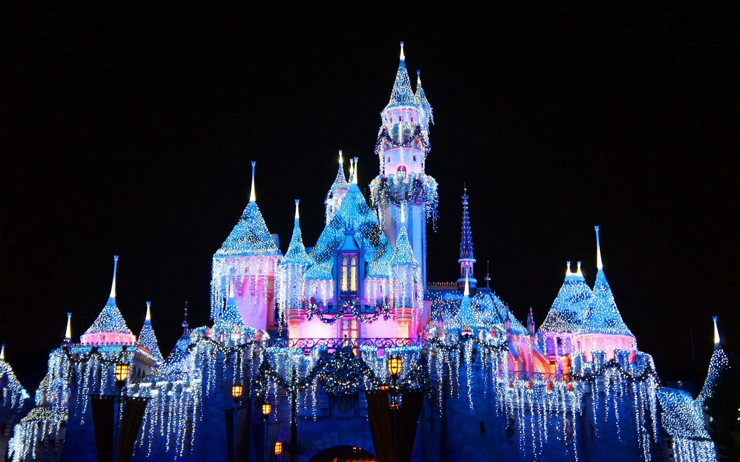 Disney World Desktop 桌布 壁紙 — 一座宏偉的城堡，裝飾著層疊的藍色和粉紅色燈光，在漆黑的夜空中閃耀。
