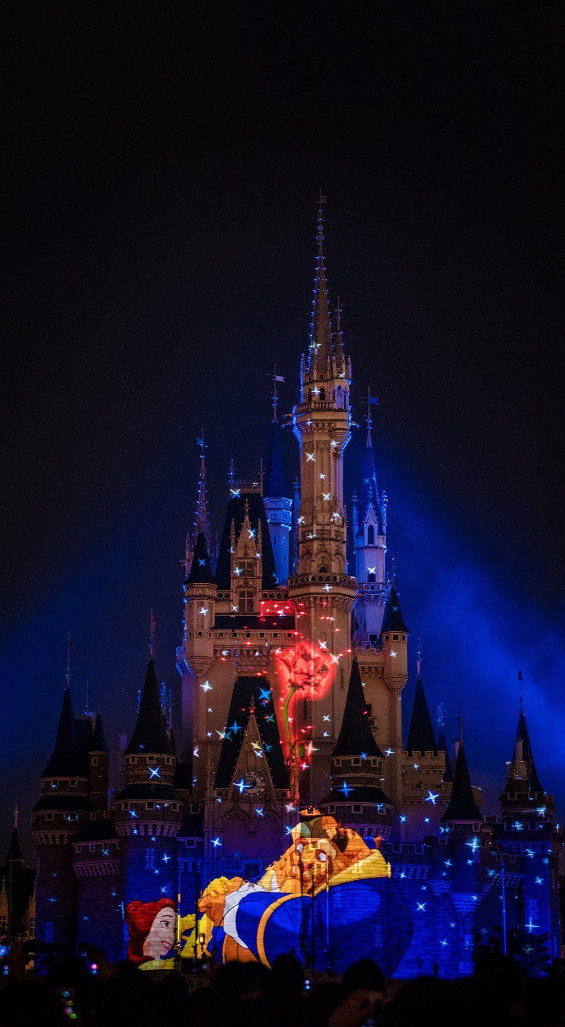 Disneyland Castle 桌布 壁紙 — 一座宏偉的城堡在夜間投影表演中，被藍色和紅色的燈光照亮，伴隨著動畫角色。