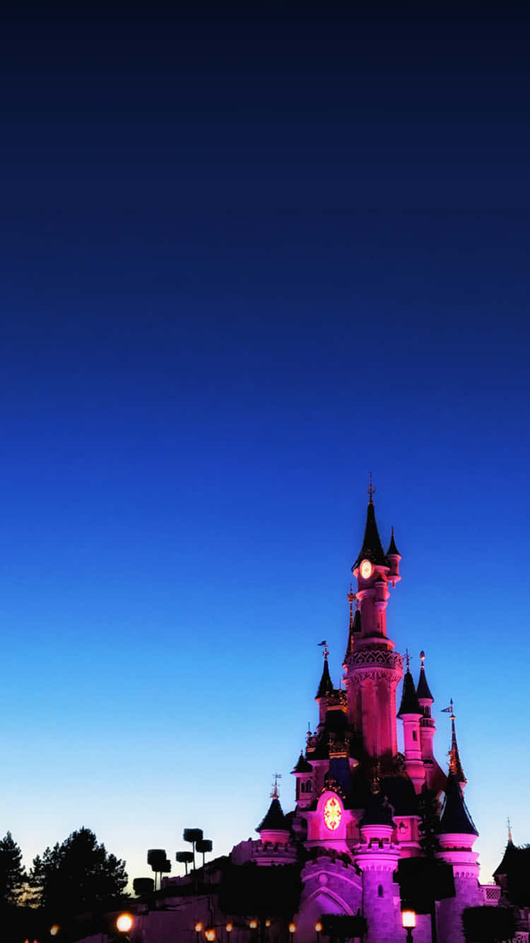 Disneyland 桌布 壁紙 — 一座宏偉的城堡在深藍色暮色天空的襯托下，被粉紅色和紫色的燈光照亮。