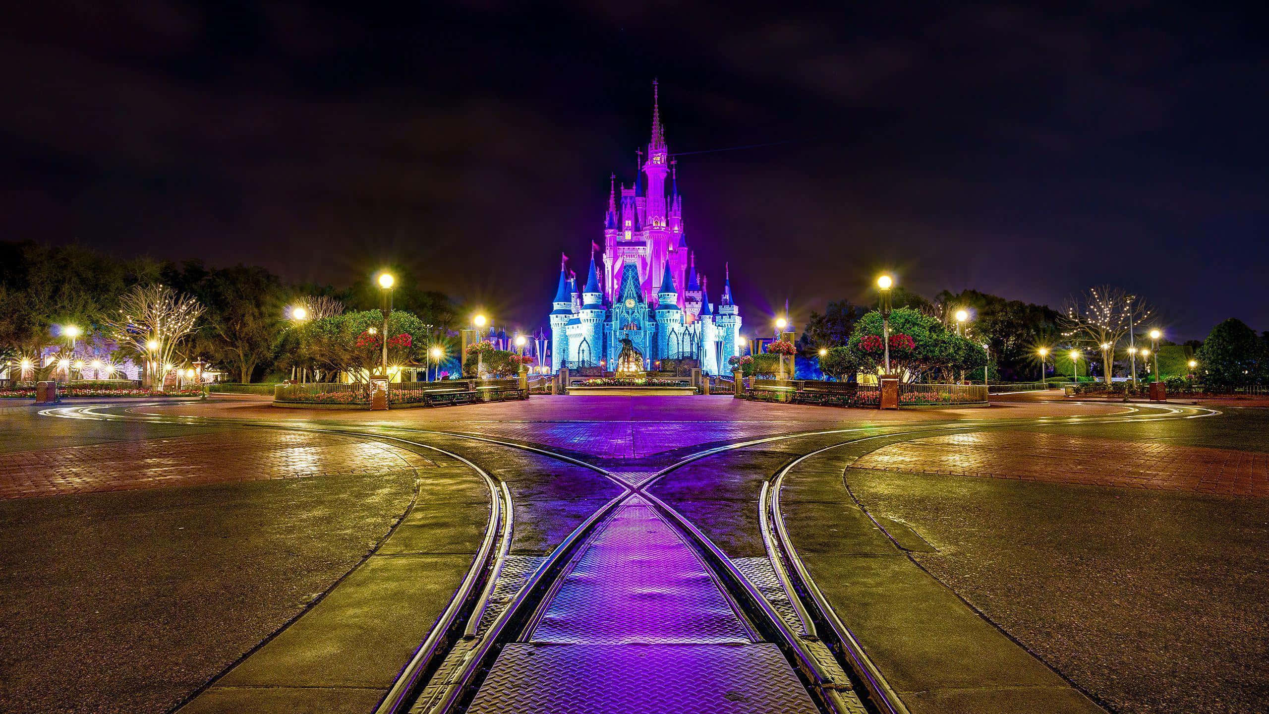 Disneyland 桌布 壁紙 — 一座宏偉的城堡在紫色和藍色燈光照射下，矗立在匯合的鐵軌盡頭，背景是漆黑的夜空。