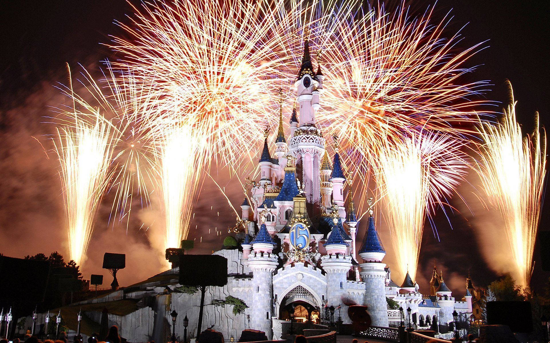 Disneyland 桌布 壁紙 — 一座宏偉的城堡被燦爛的煙火照亮，煙火在黑暗的夜空中爆發出鮮豔的橙色和金色。