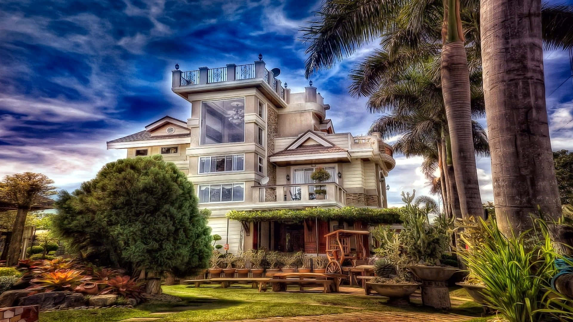 Mansion 桌布 壁紙 — 一座宏偉的多層別墅，設有陽台和棕櫚樹，矗立在晴朗藍天和縷縷白雲下。