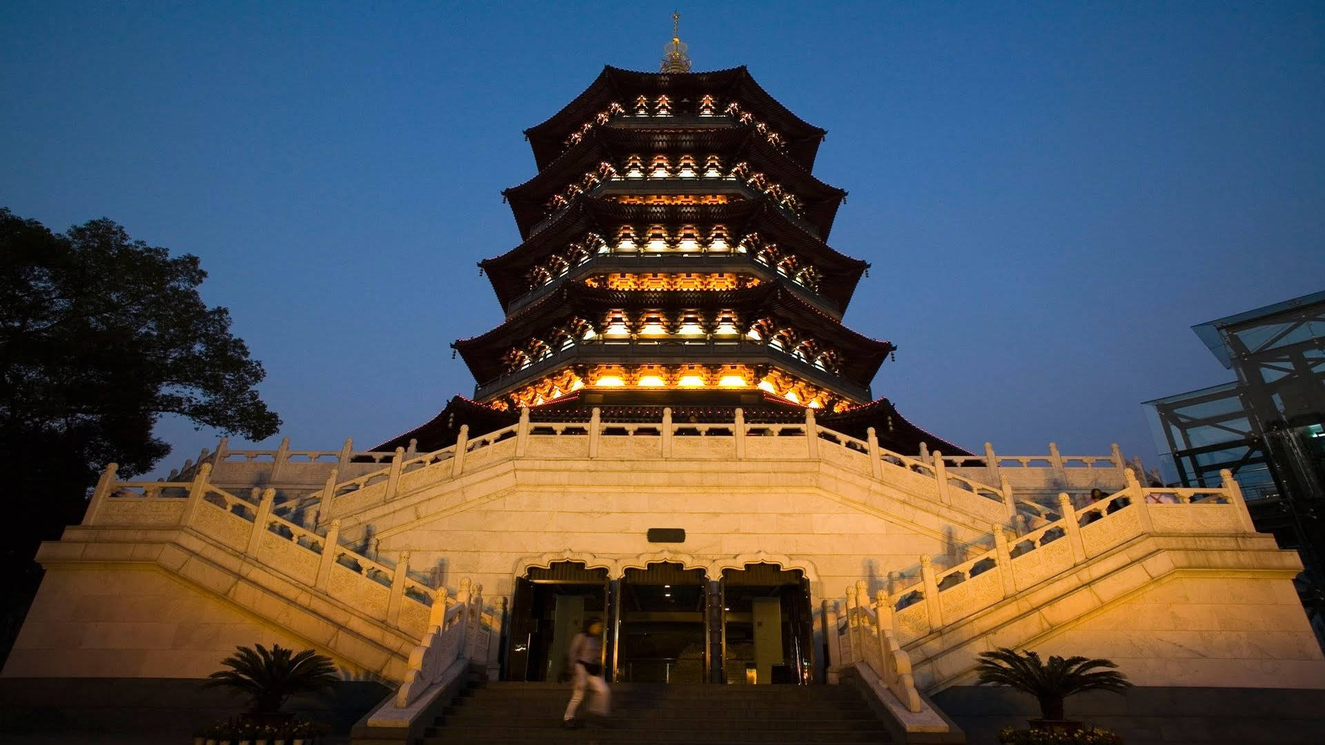 Hangzhou 桌布 壁紙 — 一座宏偉的多層寶塔在深沉的暮色中散發溫暖光芒，一人正踏上其石階。