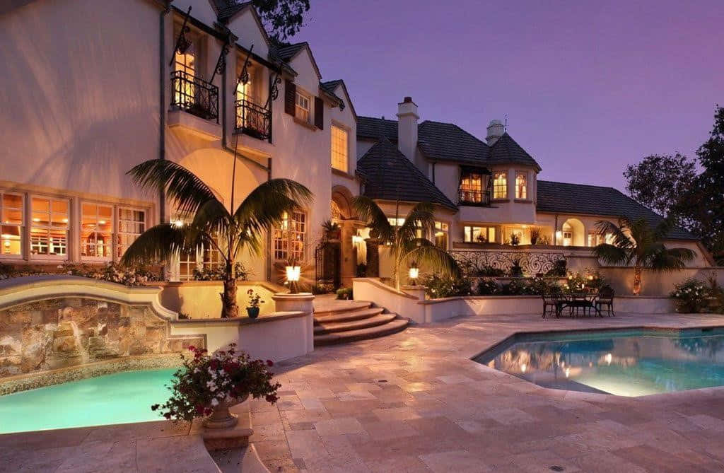 Beautiful House 桌布 壁紙 — 一座宏偉的大宅，擁有溫暖發光的窗戶和棕櫚樹，在暮色天空下矗立在閃閃發光的游泳池旁。
