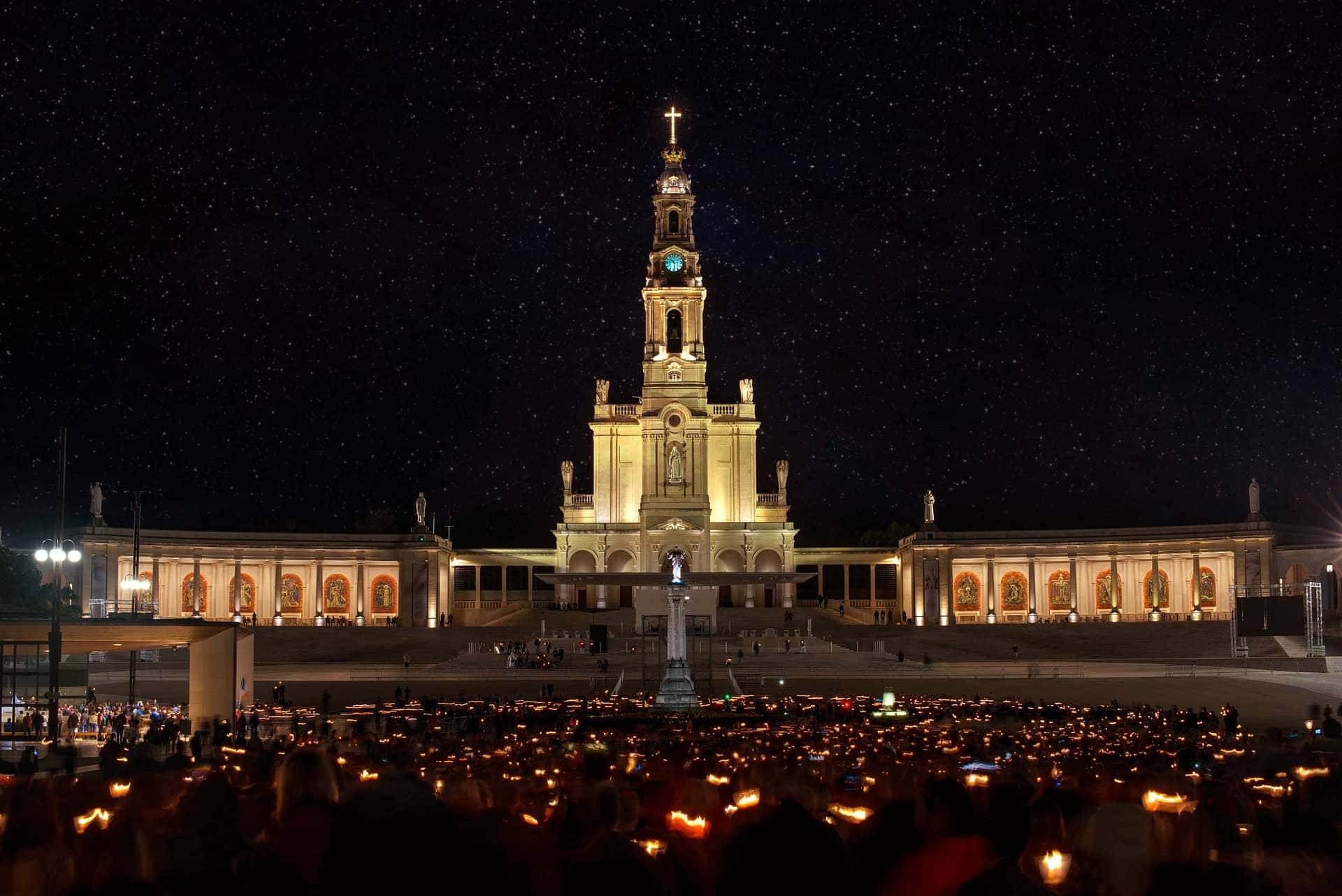 Portugal 桌布 壁紙 — 一座宏偉的大教堂在繁星點點的夜空下被照亮，下方人山人海，手持發光的蠟燭。