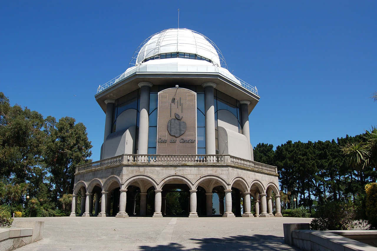 Museum 桌布 壁紙 — 一座宏偉的天文台，擁有白色圓頂和拱形柱廊，矗立在晴朗的藍天下，周圍環繞著茂密的綠樹。