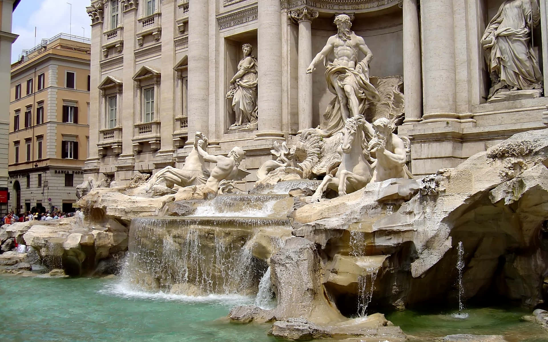 Rome 桌布 壁紙 — 一座宏偉的巴洛克式噴泉，擁有白色大理石雕像和層疊水流，位於古典建築前，天空明亮。