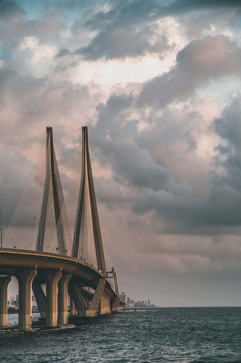 Mumbai 桌布 壁紙 — 一座宏偉的斜張橋在黃昏戲劇性的多雲天空下延伸在平靜的水面上。