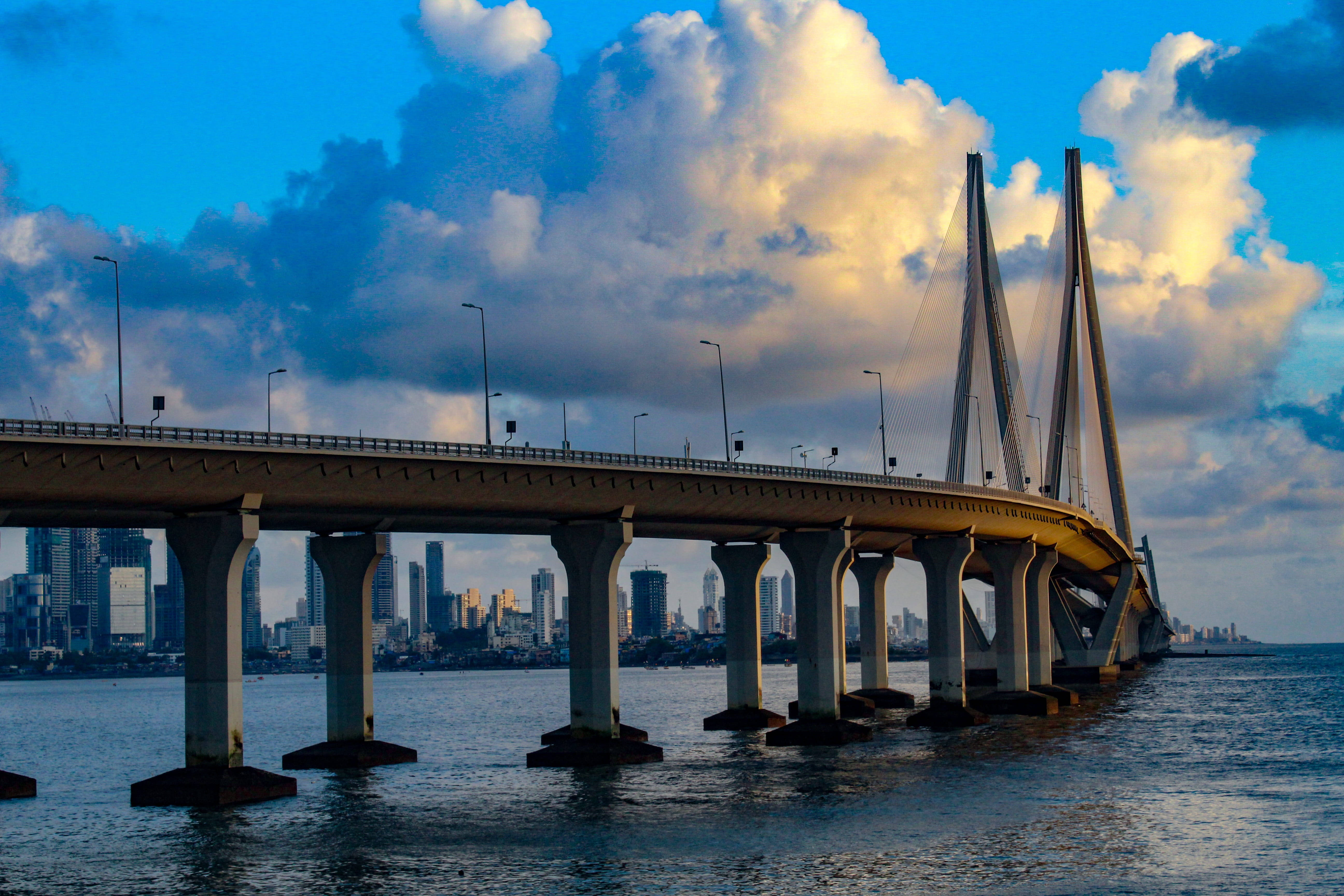 Mumbai 桌布 壁紙 — 一座宏偉的斜張橋橫跨寬闊的水道，天空壯麗，金雲密佈，遠處是城市天際線。