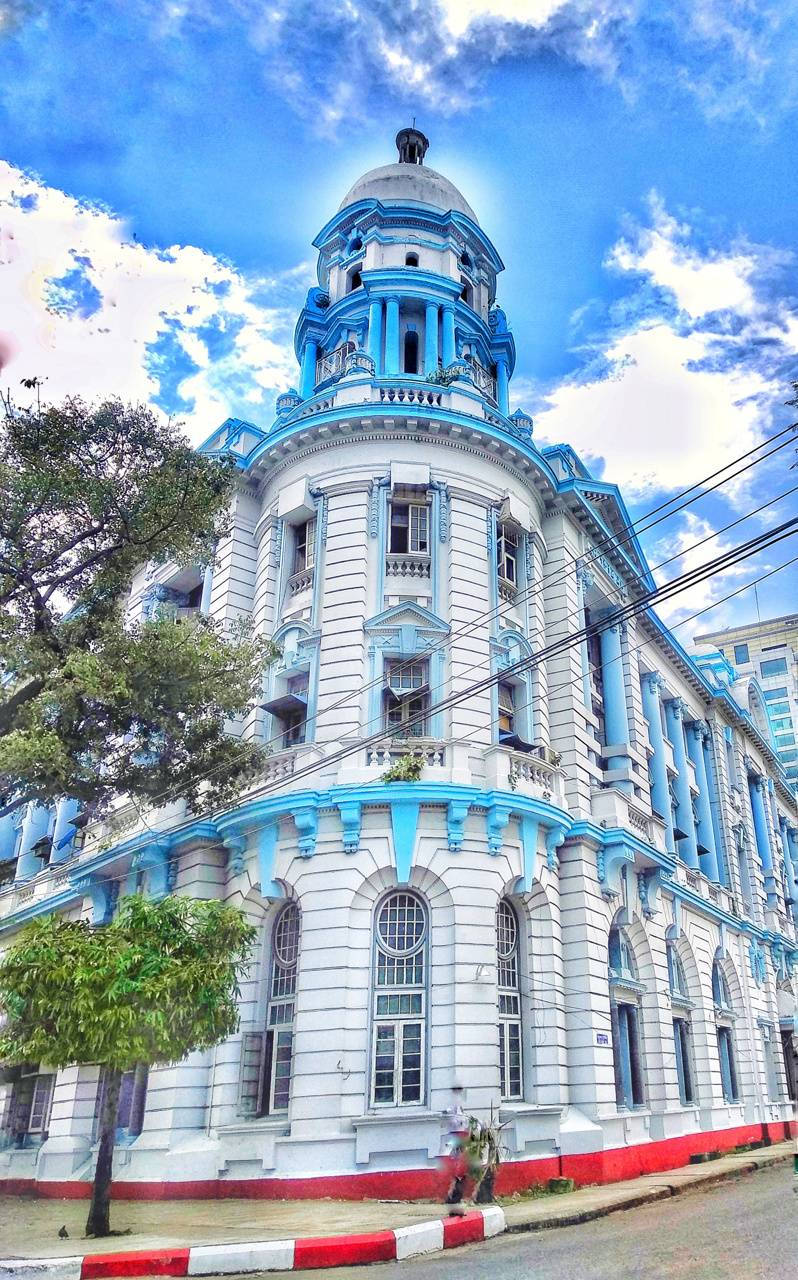 Yangon 桌布 壁紙 — 一座宏偉的新古典主義建築，帶有白色和充滿活力的藍色點綴，在藍天白雲下高高聳立。