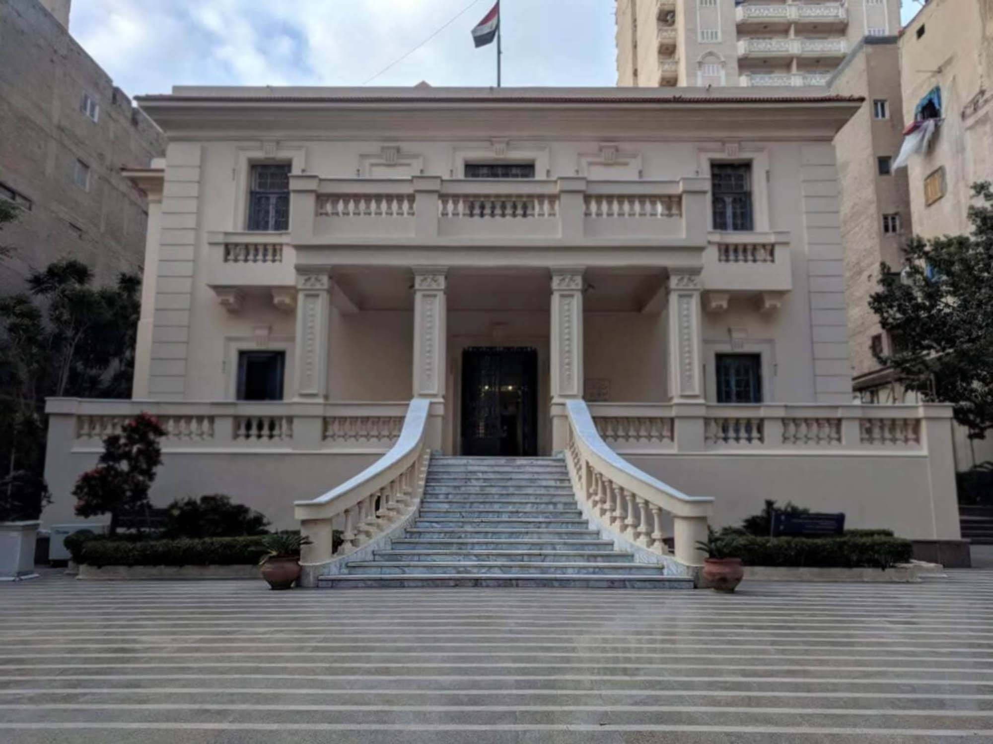 亞歷山卓 桌布 壁紙 — 一座宏偉的新古典主義建築，擁有雲石樓梯和圓柱，矗立在多雲的天空下，位於城市環境中。