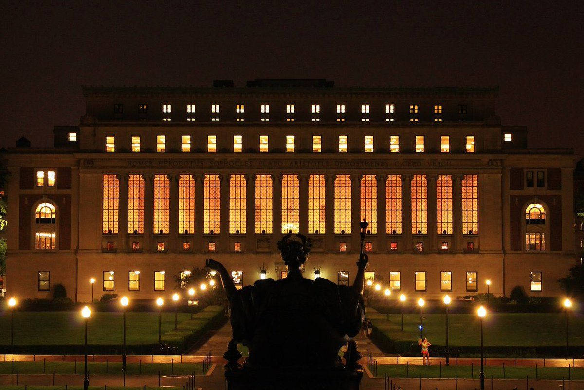 Light 桌布 壁紙 — 一座宏偉的新古典主義建築在夜晚溫暖地發光，窗戶亮著，前景有雕像剪影。