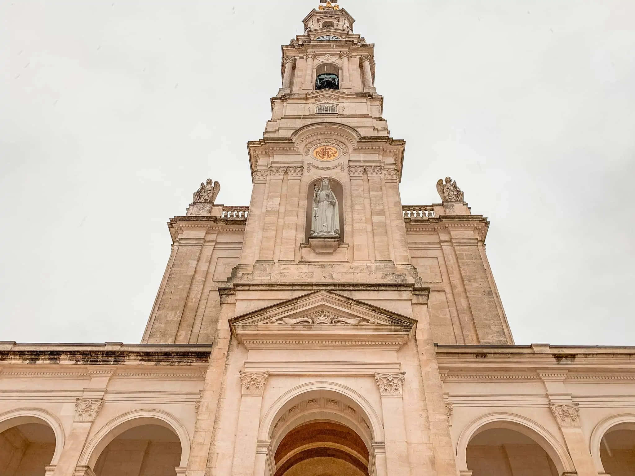 Portugal 桌布 壁紙 — 一座宏偉的新古典主義教堂塔樓在陰天升起，下方有雕像和拱形柱廊。