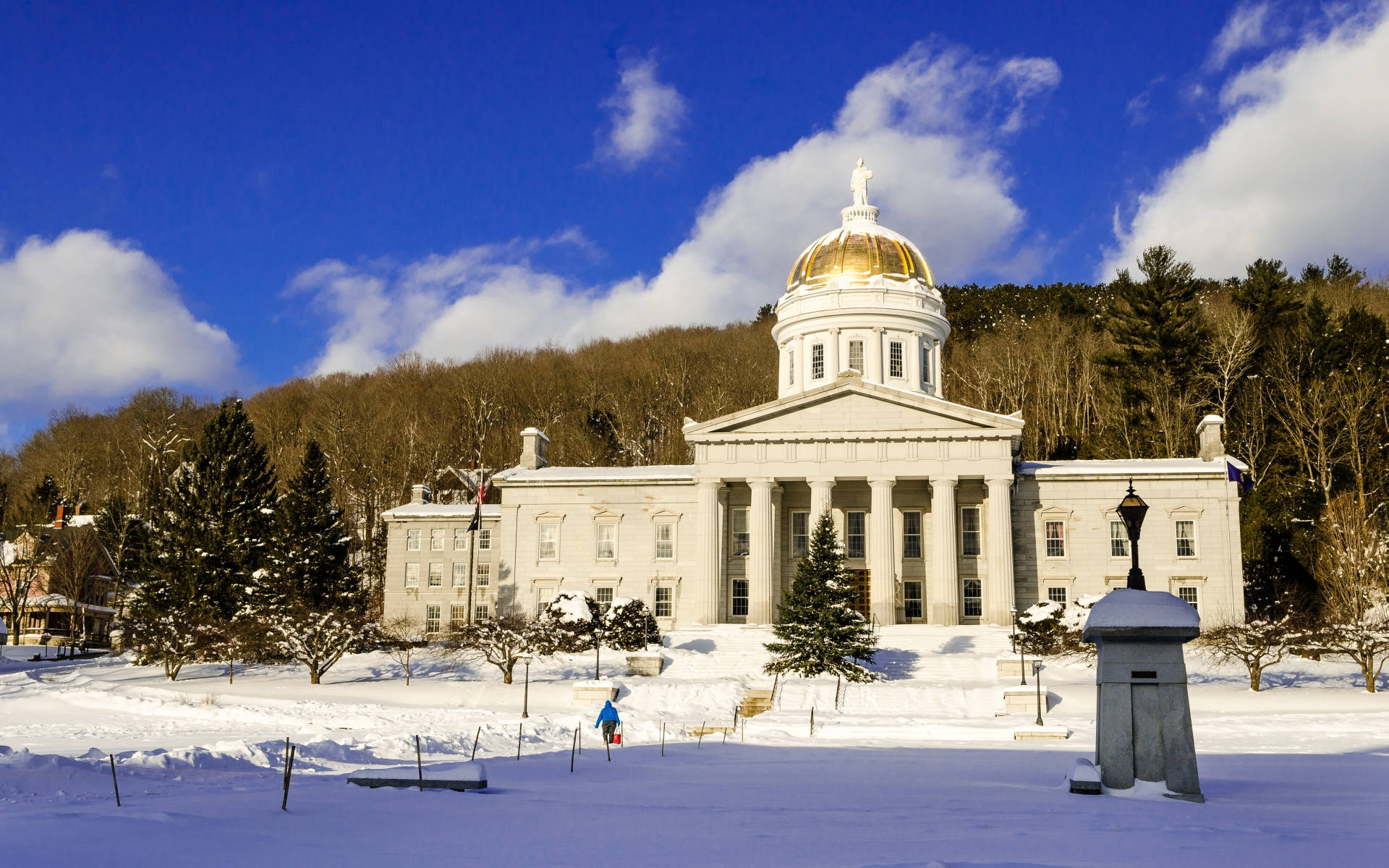 Vermont 桌布 壁紙 — 一座宏偉的新古典主義法院，金色圓頂在明亮的藍天下，矗立在白雪皚皚的冬季景觀中，氣勢磅礴。