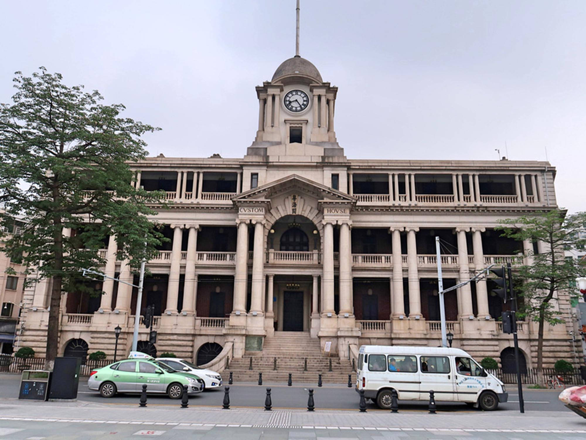 Guangzhou 桌布 壁紙 — 一座宏偉的新古典主義海關大樓，帶有鐘樓，在陰天之下巍然聳立，街道上車輛穿梭而過。