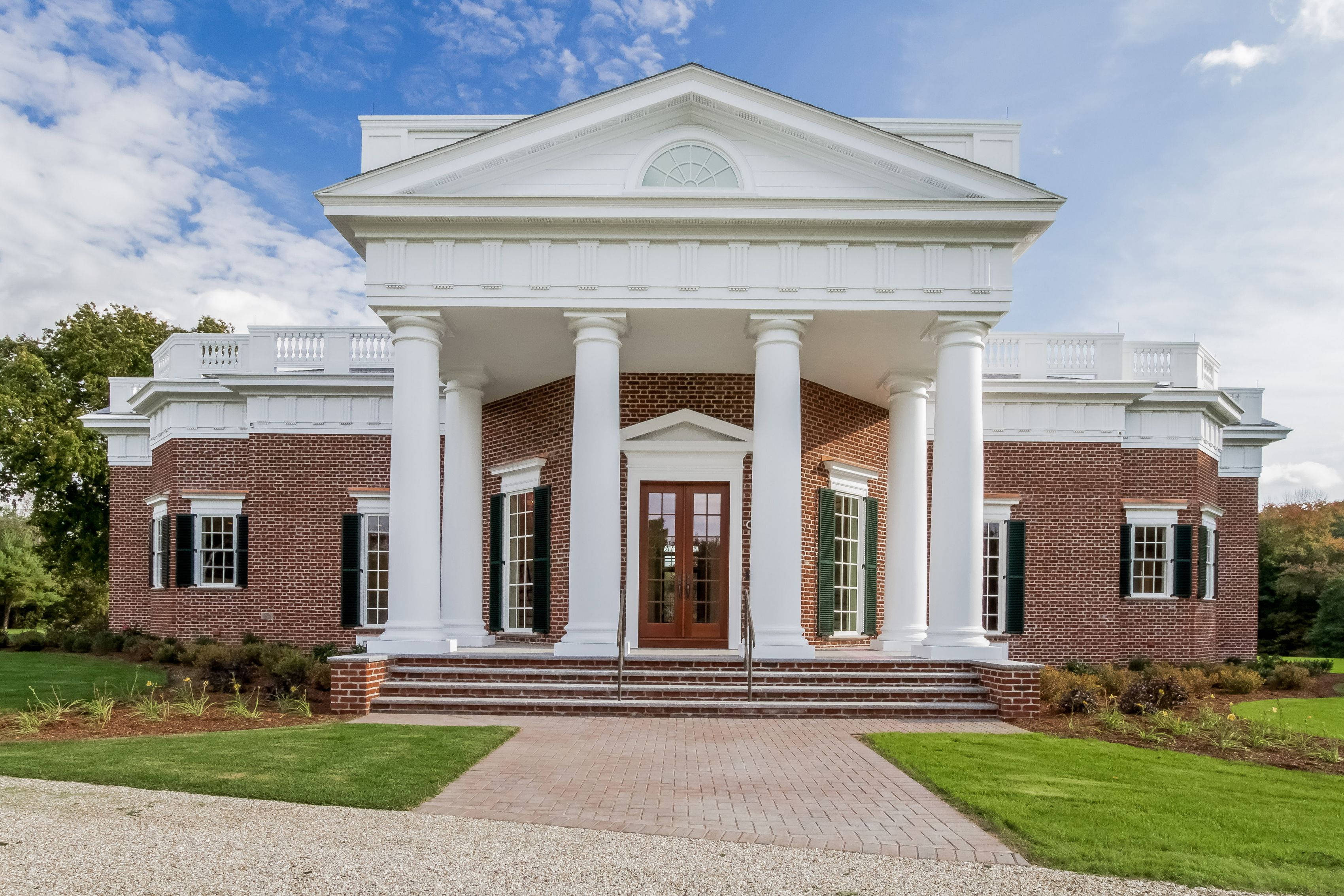 Virginia 桌布 壁紙 — 一座宏偉的新古典主義磚砌豪宅，帶有白色柱子和綠色百葉窗，矗立在晴朗的藍天下，白雲朵朵。